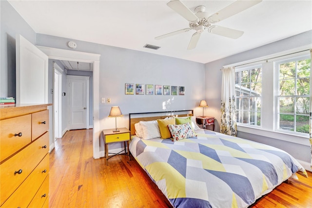 bedroom with light wood-type flooring, ceiling fan, visible vents, and attic access