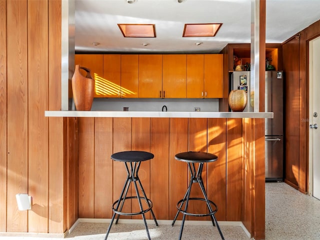 kitchen with a breakfast bar area, stainless steel fridge, kitchen peninsula, and wooden walls