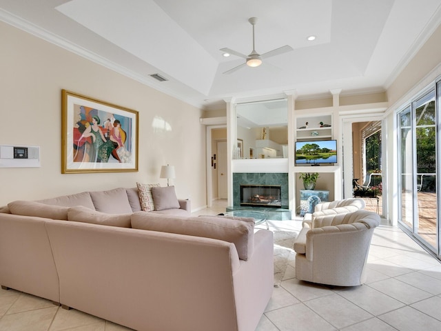 tiled living room with built in shelves, ceiling fan, a high end fireplace, and a tray ceiling