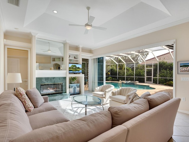 living room featuring a tray ceiling, ceiling fan, crown molding, light tile patterned floors, and a fireplace