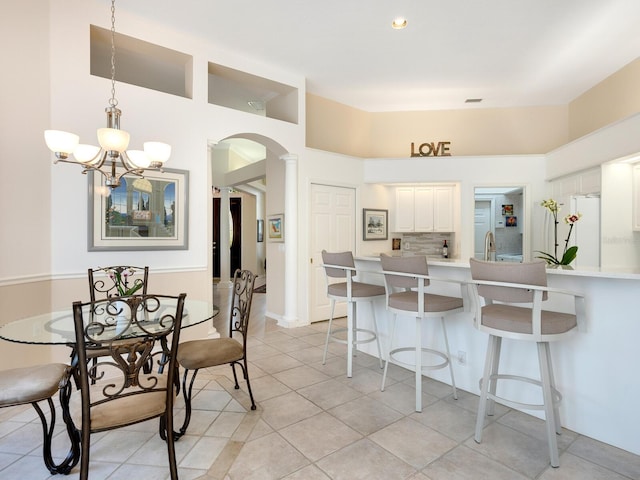 tiled dining room featuring ornate columns, a towering ceiling, sink, and an inviting chandelier