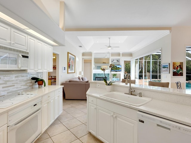 kitchen with white appliances, sink, light tile patterned floors, a tray ceiling, and white cabinetry