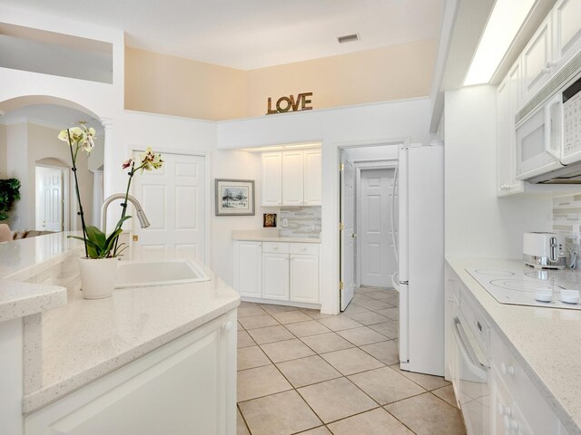 kitchen with white appliances, white cabinetry, light stone counters, and backsplash