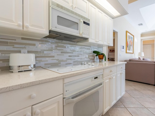 kitchen featuring backsplash, light stone counters, white appliances, light tile patterned floors, and white cabinetry