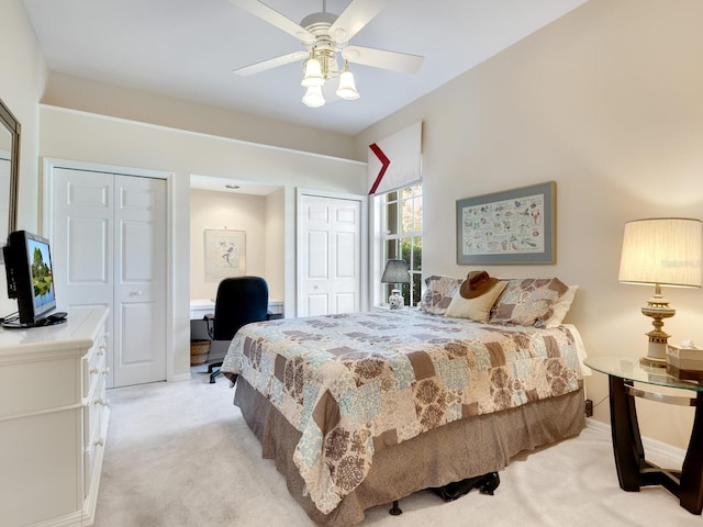 bedroom featuring ceiling fan, light colored carpet, and two closets