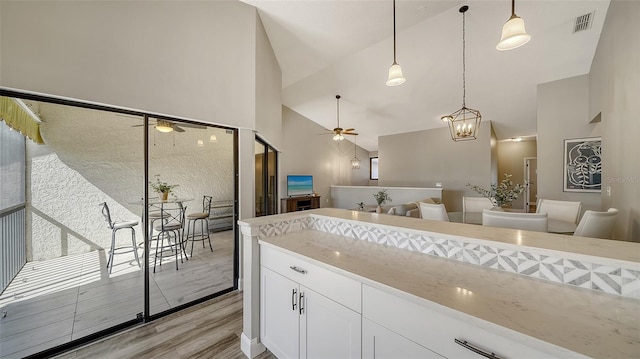 kitchen featuring ceiling fan, white cabinetry, hanging light fixtures, light stone counters, and light hardwood / wood-style floors