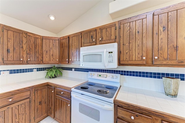 kitchen with backsplash, white appliances, vaulted ceiling, light tile patterned floors, and tile counters