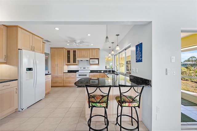 kitchen featuring a breakfast bar, glass insert cabinets, a sink, dark stone countertops, and white appliances