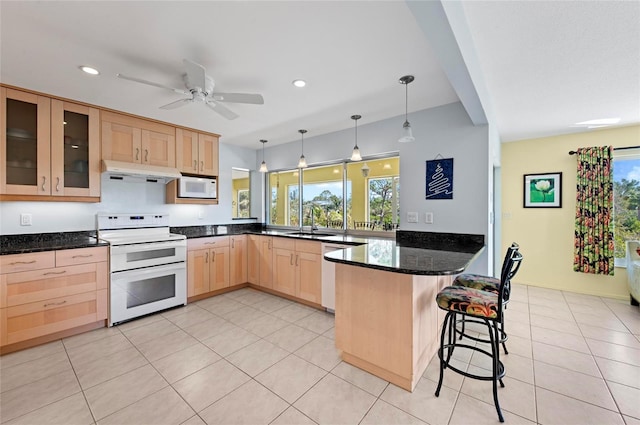 kitchen featuring light brown cabinets, under cabinet range hood, a peninsula, white appliances, and dark stone counters