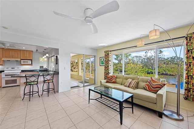 living room featuring a water view, a ceiling fan, and light tile patterned flooring