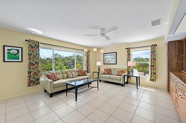 living room featuring a textured ceiling, light tile patterned floors, visible vents, and a ceiling fan