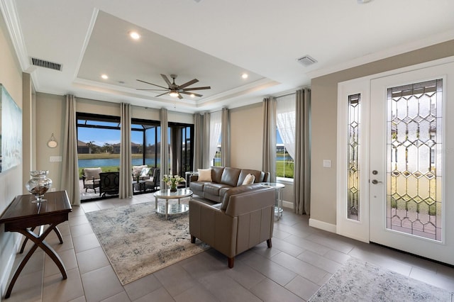 tiled living room with a raised ceiling, a water view, and a healthy amount of sunlight