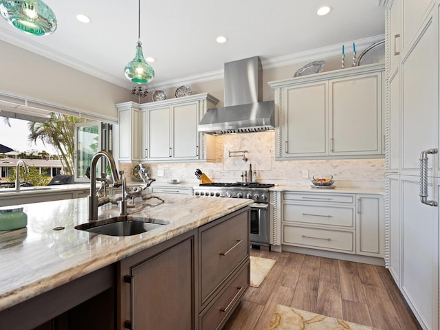 kitchen with wall chimney range hood, sink, high end stove, light stone countertops, and decorative light fixtures