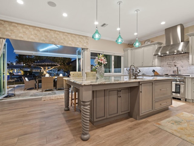 kitchen with high end stainless steel range oven, hanging light fixtures, a large island with sink, and wall chimney exhaust hood