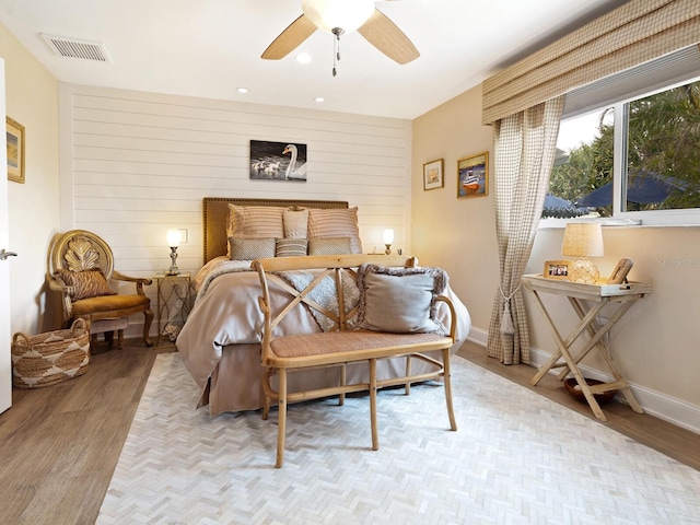 bedroom with ceiling fan, light hardwood / wood-style flooring, and wood walls