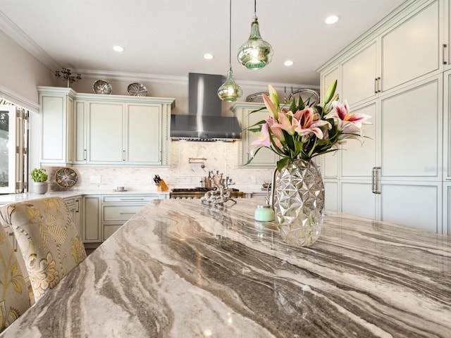 kitchen featuring light stone counters, ornamental molding, pendant lighting, wall chimney range hood, and backsplash