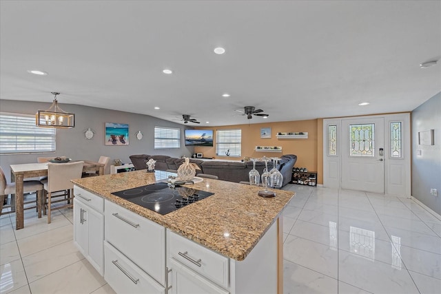 kitchen featuring light stone countertops, a center island, decorative light fixtures, black electric stovetop, and white cabinets