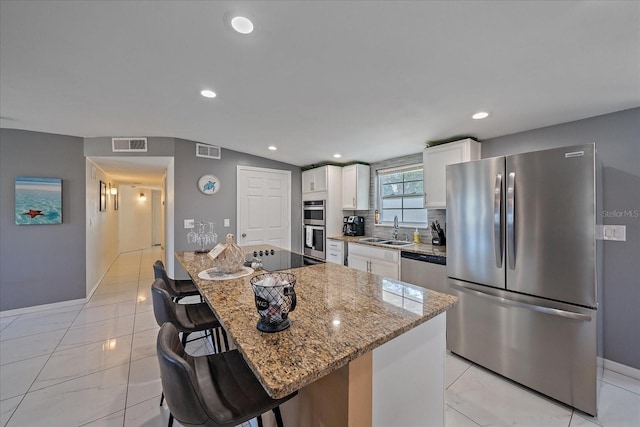 kitchen featuring appliances with stainless steel finishes, light stone counters, white cabinets, a kitchen island, and a breakfast bar area