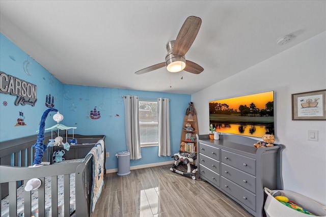 bedroom featuring vaulted ceiling, ceiling fan, a crib, and light wood-type flooring