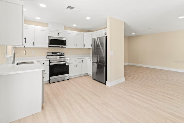 kitchen featuring appliances with stainless steel finishes, light wood-type flooring, white cabinetry, and sink