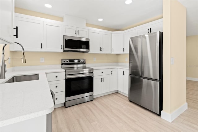 kitchen with light stone countertops, white cabinetry, sink, stainless steel appliances, and light wood-type flooring