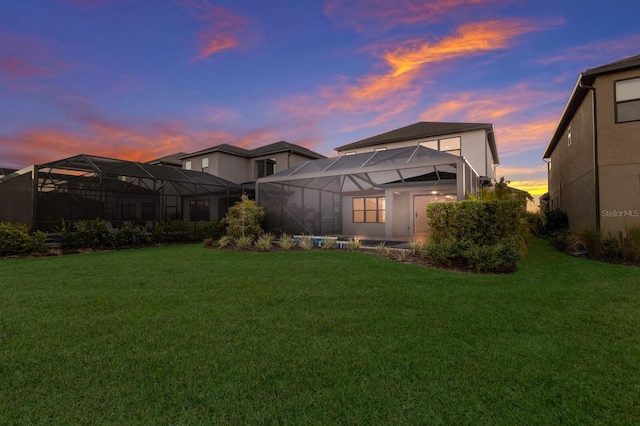 back house at dusk featuring a lanai and a yard