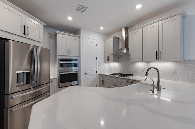 kitchen with white cabinetry, stainless steel appliances, decorative backsplash, and wall chimney range hood