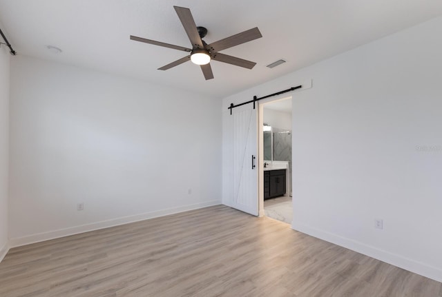 unfurnished room featuring ceiling fan, a barn door, and light wood-type flooring