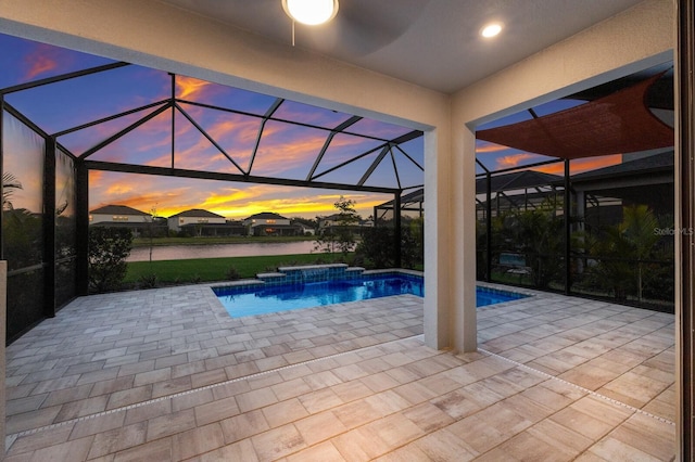 pool at dusk with a hot tub, a water view, a patio area, and a lanai