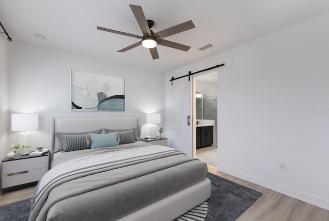 bedroom with ensuite bathroom, a barn door, ceiling fan, and light hardwood / wood-style floors