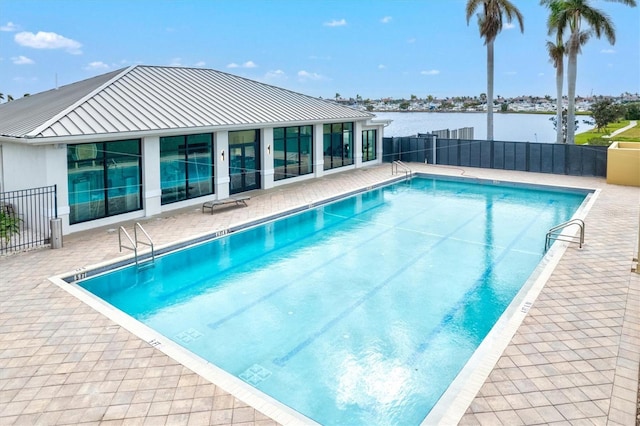 pool with a patio area, a water view, and fence