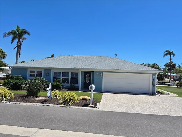 ranch-style house with an attached garage, a shingled roof, stucco siding, and decorative driveway