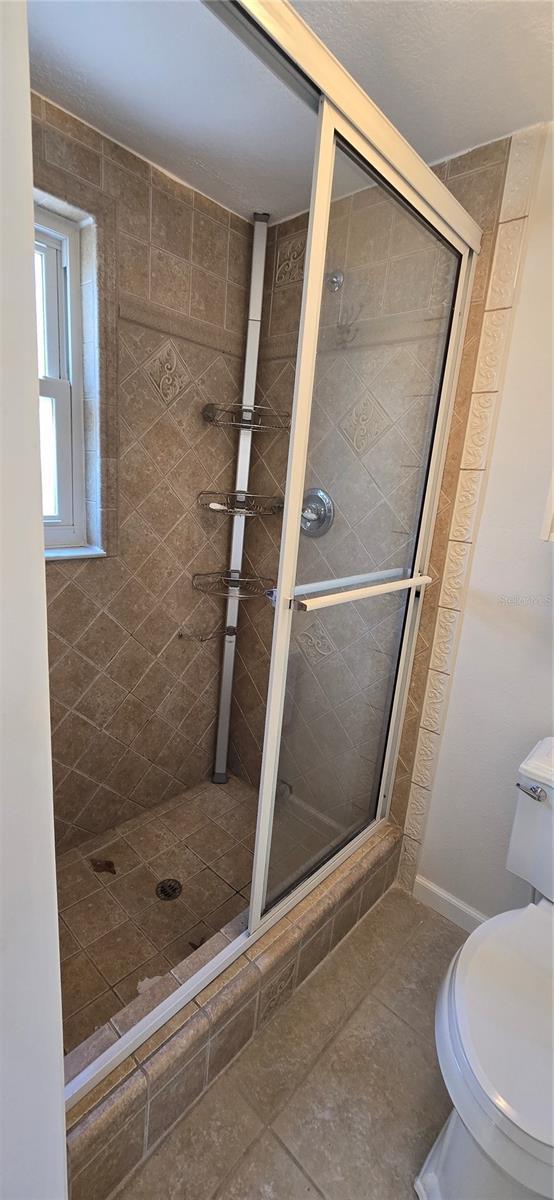 bathroom with toilet, tile patterned flooring, and a stall shower