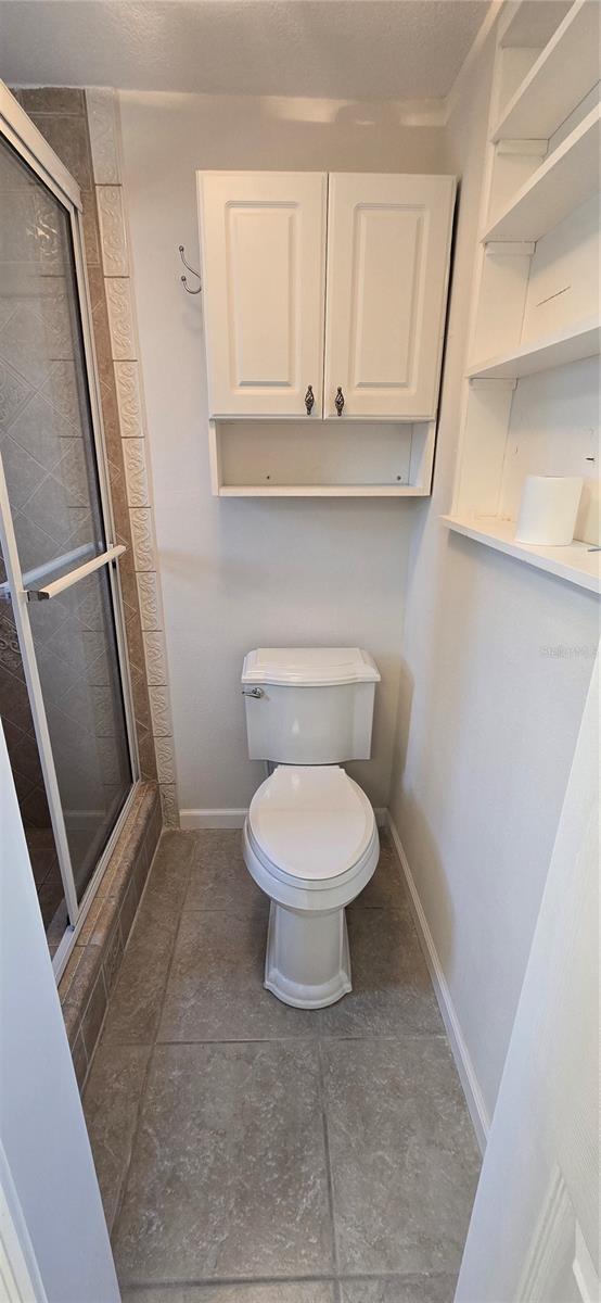 bathroom with toilet, a stall shower, baseboards, and tile patterned flooring