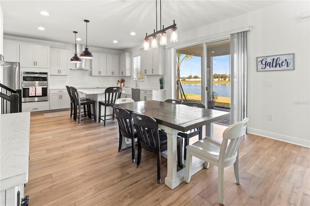 dining area featuring light wood-type flooring, a water view, and sink