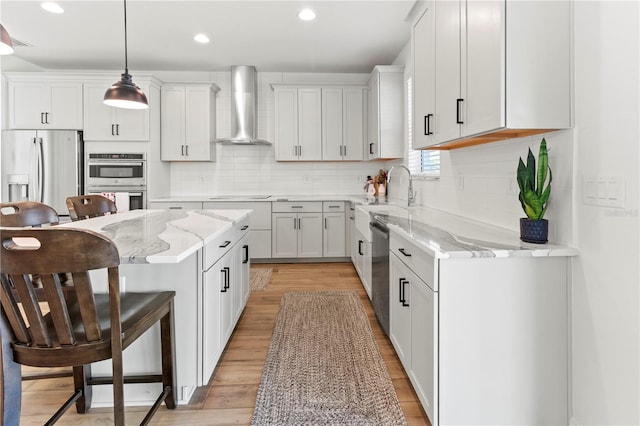 kitchen featuring pendant lighting, wall chimney range hood, appliances with stainless steel finishes, and white cabinetry