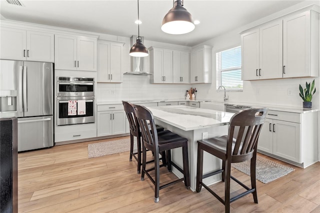 kitchen with appliances with stainless steel finishes, white cabinets, a kitchen island, light hardwood / wood-style flooring, and pendant lighting