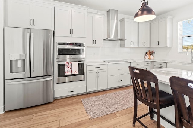 kitchen featuring appliances with stainless steel finishes, decorative light fixtures, white cabinetry, wall chimney range hood, and sink