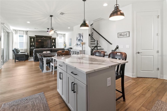 kitchen featuring a kitchen breakfast bar, hanging light fixtures, light stone counters, gray cabinets, and a center island