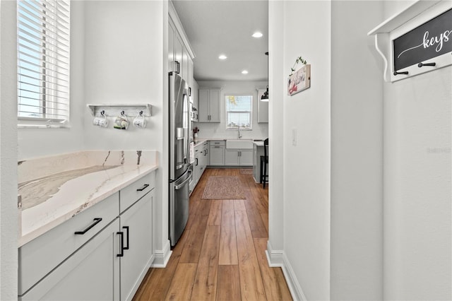 kitchen featuring light stone countertops, white cabinets, sink, and light wood-type flooring