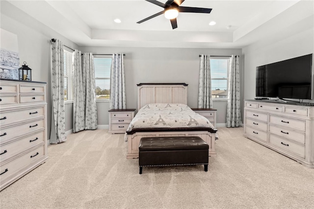 bedroom featuring multiple windows, ceiling fan, light carpet, and a tray ceiling