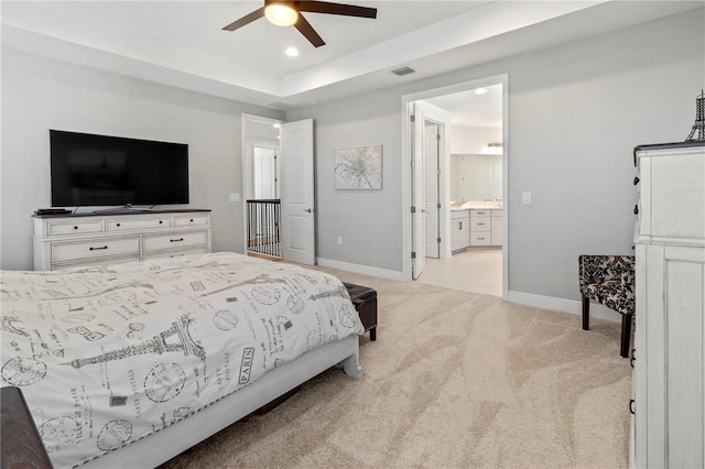 bedroom featuring ceiling fan, ensuite bathroom, a raised ceiling, and light colored carpet