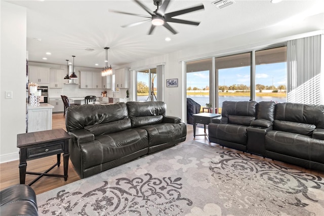 living room featuring ceiling fan with notable chandelier, a water view, and light hardwood / wood-style floors