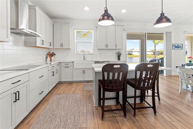 kitchen featuring pendant lighting, white cabinets, wall chimney range hood, black electric stovetop, and sink