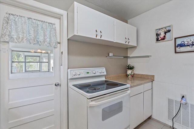 kitchen with light tile patterned floors, a textured ceiling, white cabinetry, and white electric stove