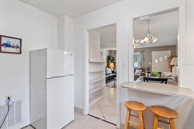 kitchen with a breakfast bar, light tile patterned floors, white refrigerator, decorative light fixtures, and a notable chandelier