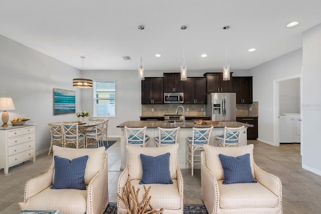 kitchen with appliances with stainless steel finishes, a breakfast bar, washer and dryer, a center island with sink, and hanging light fixtures