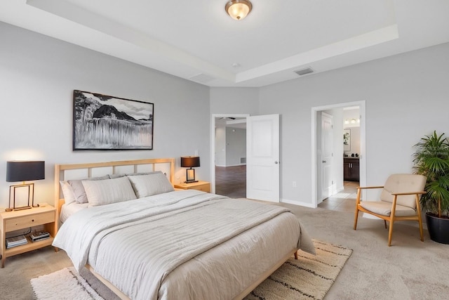 bedroom featuring a tray ceiling, ensuite bath, and carpet floors