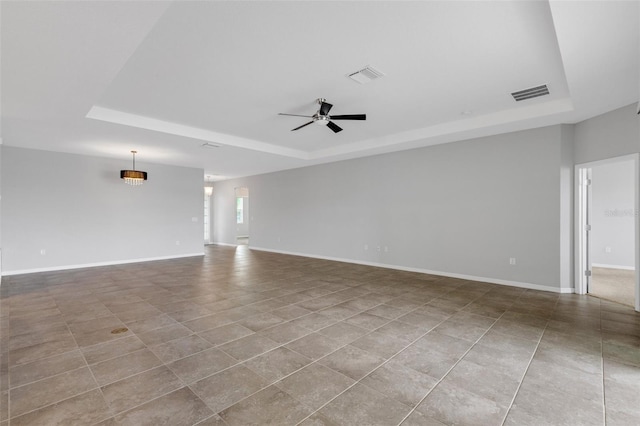 empty room with ceiling fan, a raised ceiling, and light tile patterned floors