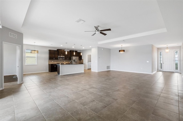 unfurnished living room with a raised ceiling, ceiling fan, and sink